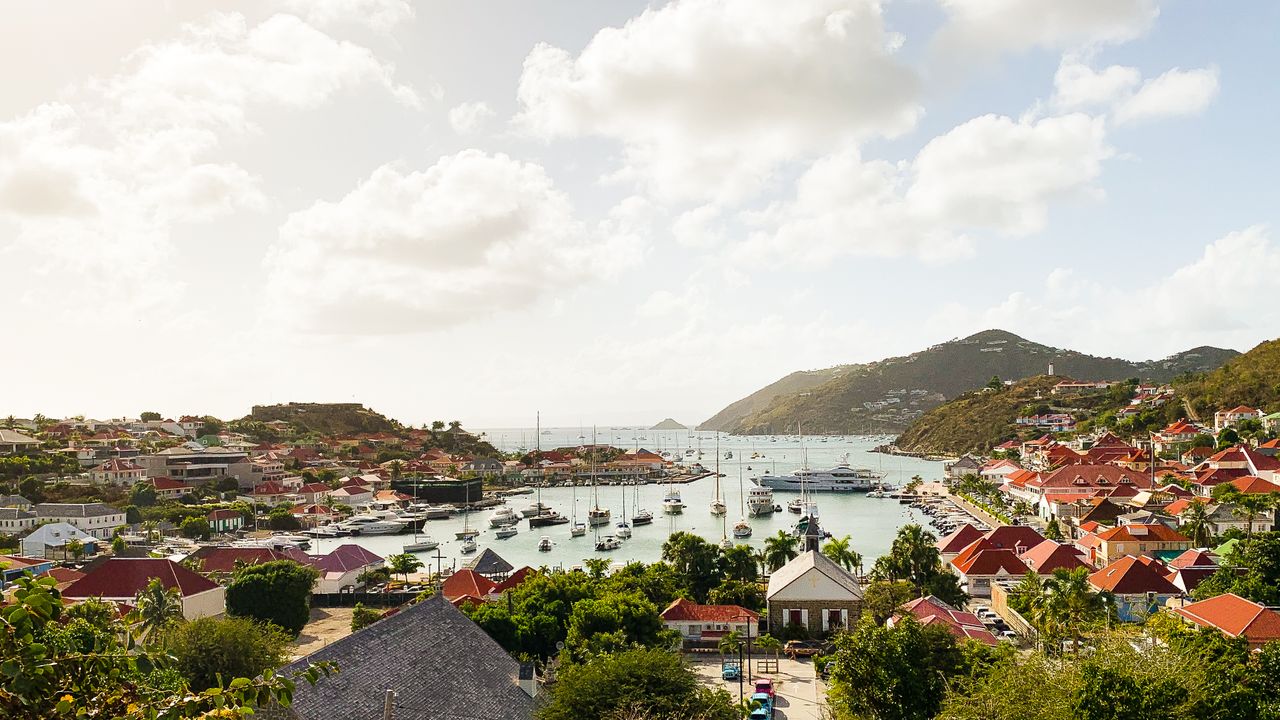 Best eSIM for Saint Martin; a scenic coastal harbor town in Saint Martin with red-roofed houses, boats in the water, green hills, and a bright cloudy sky.