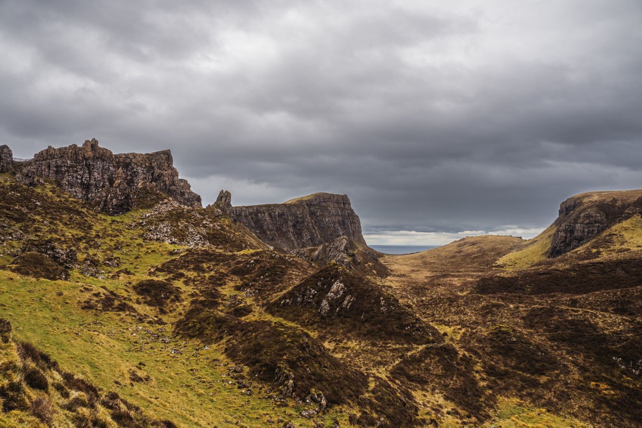 Best Scotland eSIM for travel; a mountain landscape in Scotland with steep rocky cliffs, grassy slopes, and a cloudy gray sky overhead.