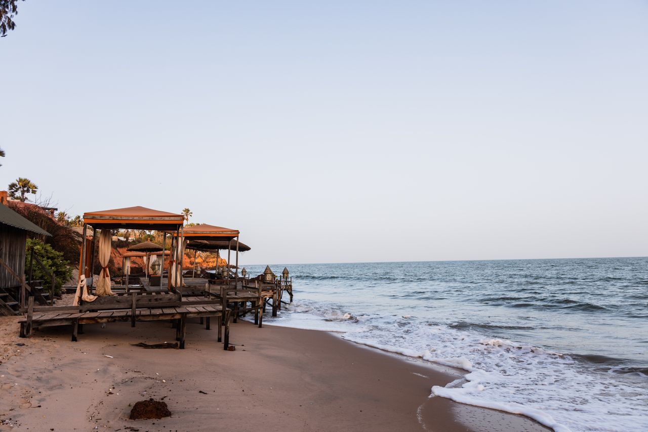 Best Senegal eSIM; a beachfront scene in Senegal with wooden cabana-style beach umbrellas and lounge seating on a sandy shore, with gentle waves rolling in from the ocean.