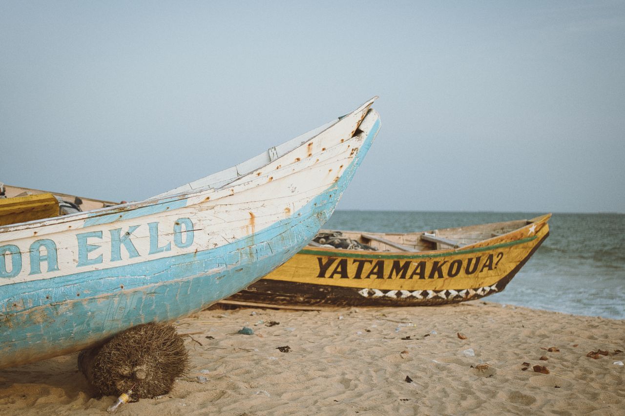 Best eSIM for Senegal; two weathered fishing boats in Senegal resting on a sandy beach near the ocean under a pale sky.