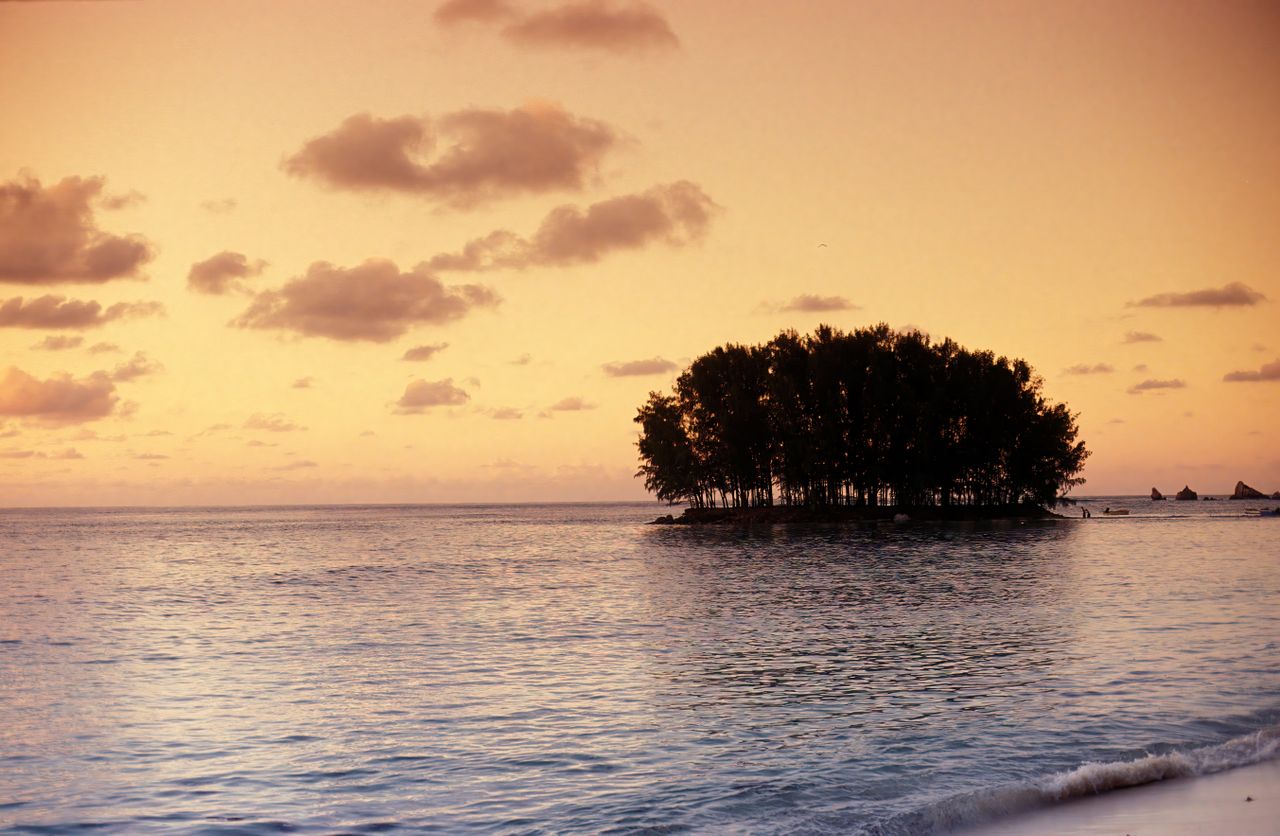 Best Seychelles eSIM for travel; a scenic sunset seascape in the Seychelles with calm blue water, a small tree-covered island at center-right.