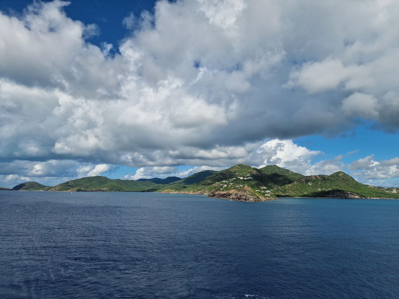Best St. Kitts and Nevis eSIM for travel; a scenic view of a blue ocean with green mountains in the distance under a cloudy sky.