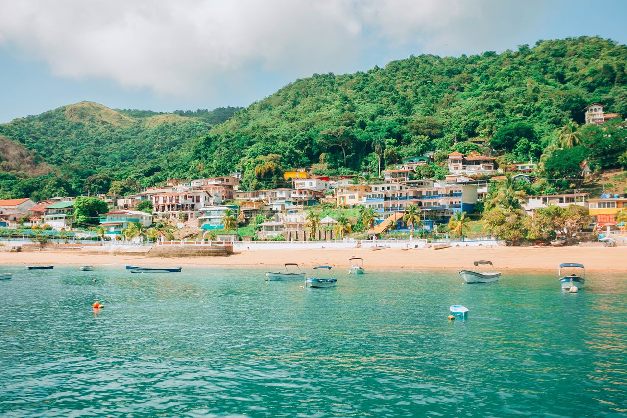 Best Saint Lucia eSIM for travel; a scenic coastal landscape in Saint Lucia with turquoise water, small boats on the beach, a sandy shoreline, and a hillside village with colorful buildings.