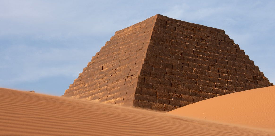 Best eSIM for Sudan; a low-angle photograph of a large stone pyramid in Sudan rising from a sandy desert.