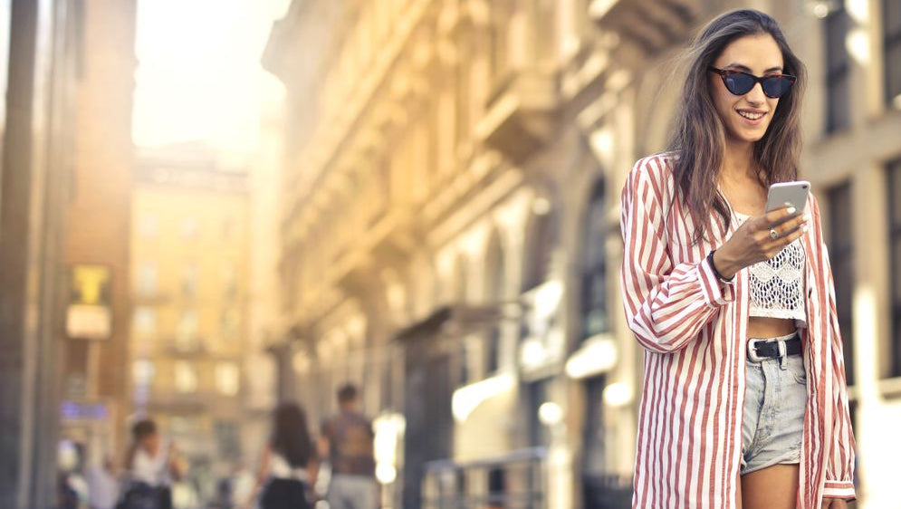About Always Mobile; female tourist with phone in European street with sun shining down.