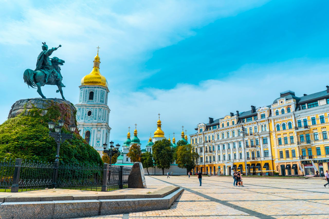 Best eSIM for Ukraine travel; photo of a scenic view of a city square in Ukraine with a large equestrian statue in the foreground, a white church tower with a golden dome, colorful historic buildings on the right.