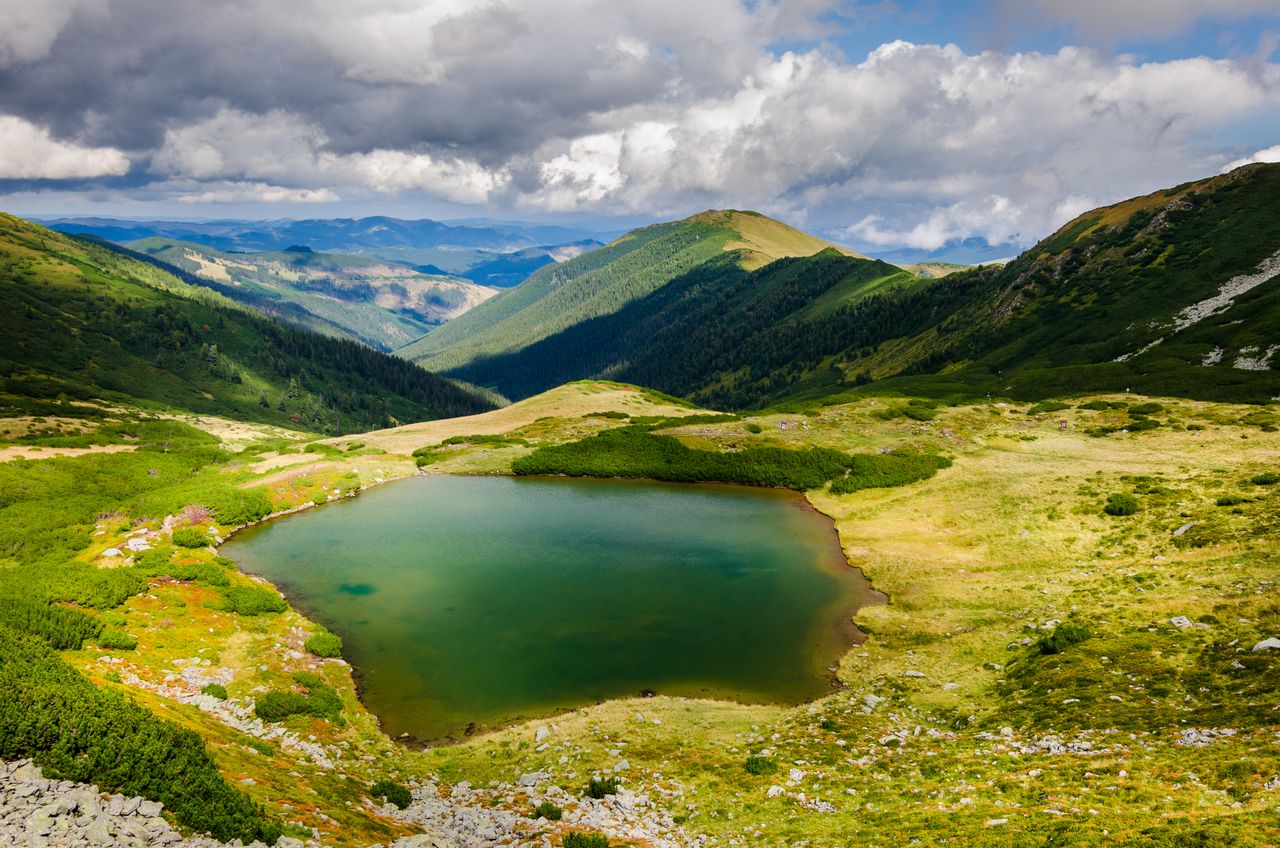 Best Ukraine eSIM for travel; photo of a scenic mountain landscape in Ukraine with a small green lake in the foreground, surrounded by grassy slopes and rugged peaks.