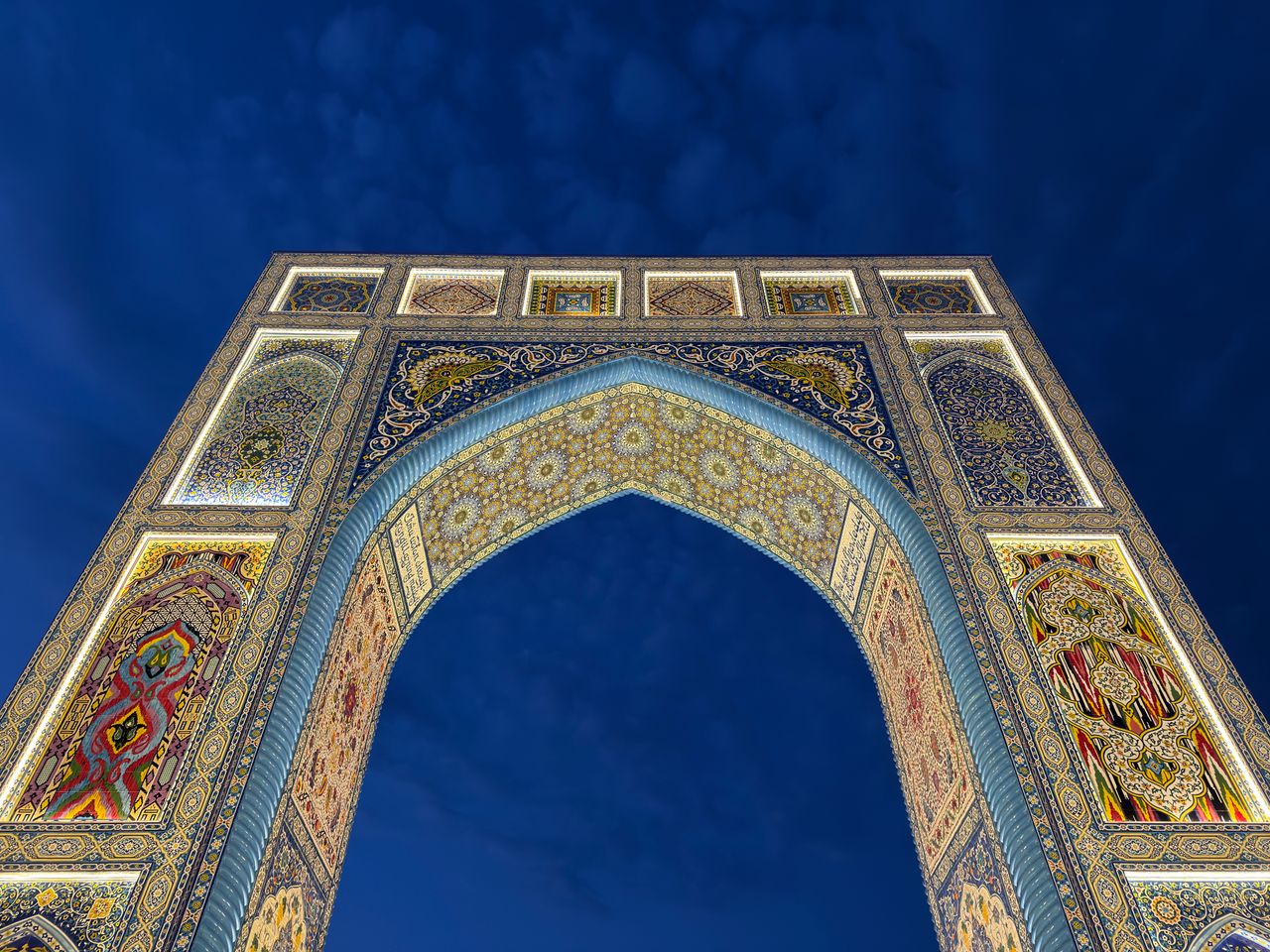 Best Uzbekistan eSIM for travel; an ornate arched gateway in Uzbekistan with intricate mosaic tilework in blue, gold, and red, photographed against a deep blue sky.