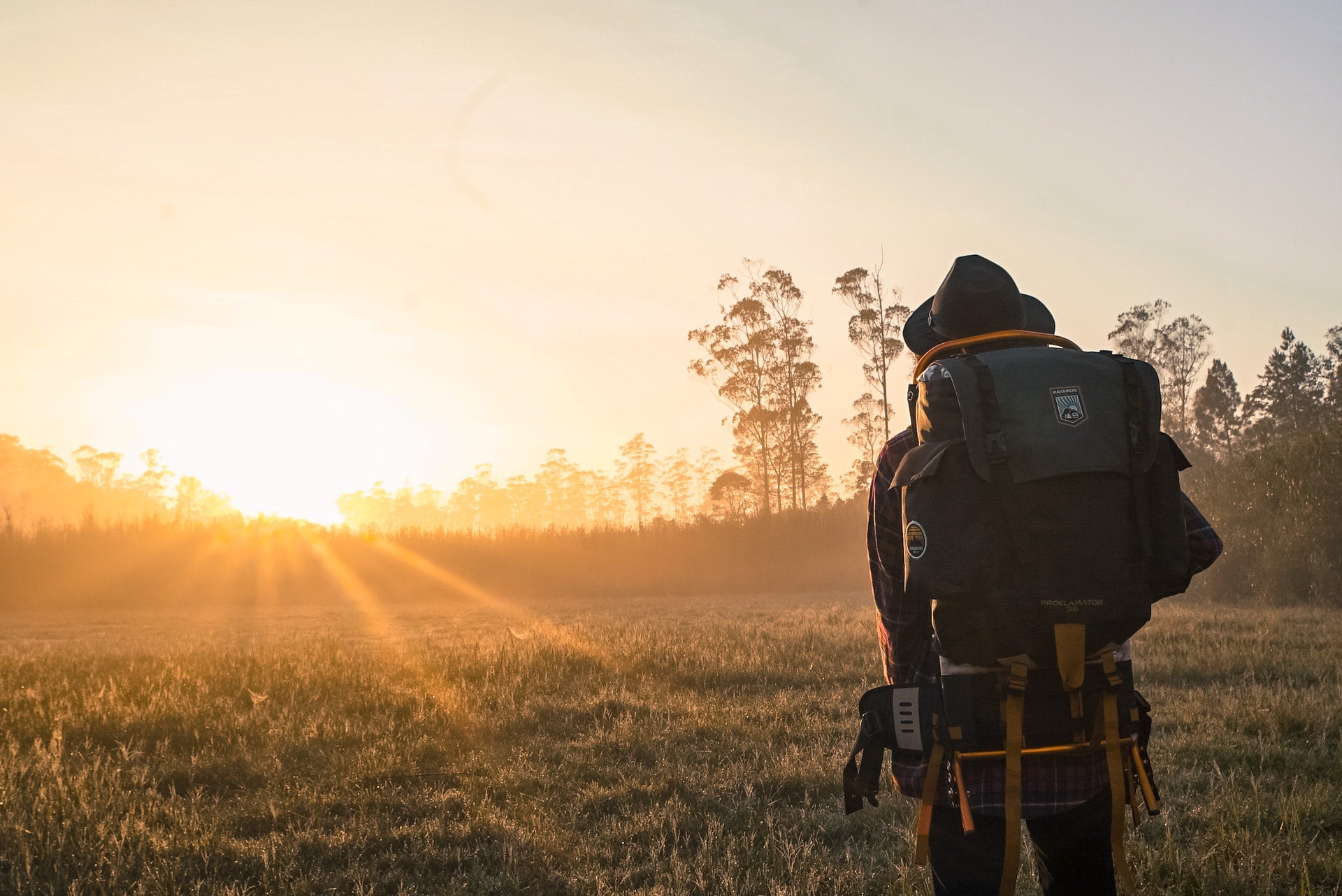 About Always Mobile; a backpacker at dawn watching the sun rise over a grassy field with trees in the background